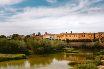Old city buildings and lush green vegetation lining the Guadalquivir river in Cordoba, Andalucia, Spain