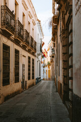 Ancient architecture lining a quiet, winding alleyway in Andalucia's historic city, featuring a Spanish flag