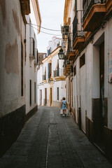 Fototapeta premium Woman walking along a traditional narrow street in the historic Jewish Quarter of Cordoba, Andalucia. Exploring Spanish old town alleyways