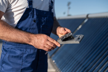 Worker standing near modern solar energy equipment on roof