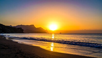 Golden sun dips below the horizon, painting a beach in warm light with mountains silhouetted in the distance