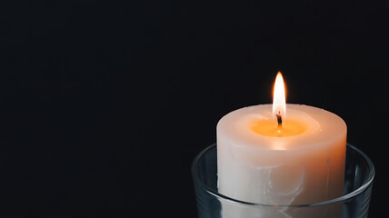 White Pillar Candle Burning in a Glass Holder on Black Background flame light