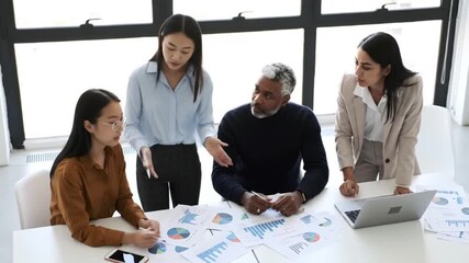 Four diverse business professionals collaborating on financial data and charts in a modern office meeting. - Powered by Adobe