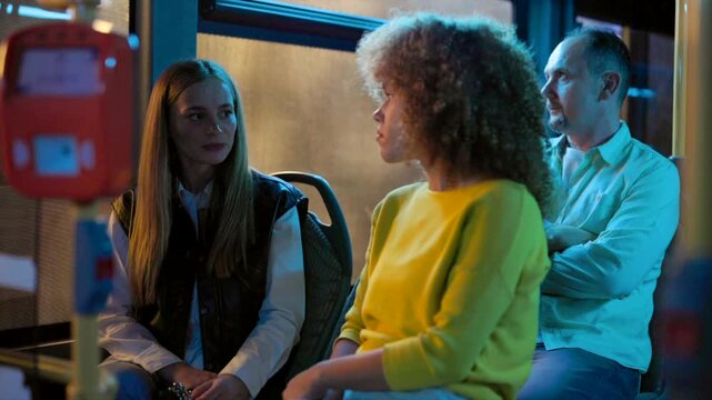 Diverse young female friends having a heartfelt conversation while traveling on a bus during their nightly commute, sharing stories and enjoying their journey through the illuminated city streets