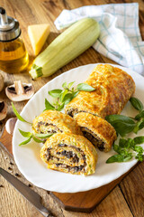 Zucchini roll with mushroom filling and herbs served on a white plate on a rustic table.