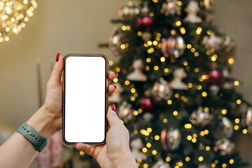 Mockup woman's hand holding using smart phone with white blank screen at Christmas light background, mobile app design and advertising, online marketing