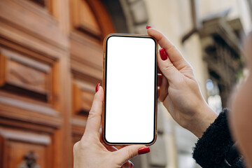 Mockup woman's hand holding using smart phone, Hands are holding a smartphone featuring a blank screen, positioned in front of a wooden door, real estate rent, mobile app design and advertising