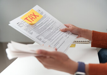 Fototapeta premium Tax filing. Individual holding tax documents and reviewing them at a desk.