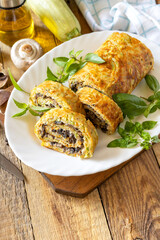 Zucchini roll with mushroom filling and herbs served on a white plate on a rustic table.