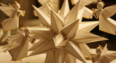 Close-up of handcrafted origami paper angels and a star ornament, adorned with gold trim, against a blurred, warm-toned festive background, creating a soft and whimsical