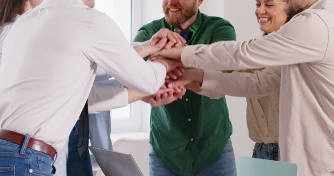 Team of happy business people celebrating starting online sales after finishing project in digital marketing technologies, stacking hands, high fiving, applauding, having fun. Teamwork success concept