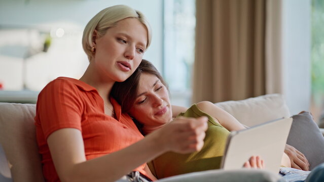 Cuddling lesbian pair talking together using tablet at home closeup. Lgbt couple
