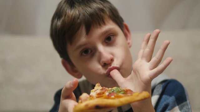 Portrait of a Caucasian boy holding a pizza and licking his fingers with pleasure, pizzeria concept, pizza delivery
