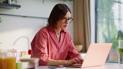 Domestic businesswoman typing laptop at light kitchen closeup. Woman thinking