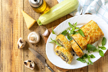 Zucchini roll with mushroom filling and herbs served on a white plate on a rustic table. Top view.