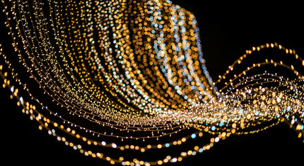 Bokeh effect of illuminated string lights creating a flowing wave pattern against a stark black background, generating a magical and festive mood.