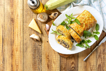 Zucchini roll with mushroom filling and herbs served on a white plate on a rustic table. Top view.