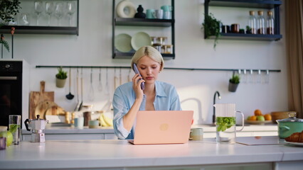 Working lady calling cellphone at kitchen closeup. Happy girl typing laptop