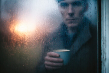 Man holding a cup behind foggy glass, illuminated by warm evening light