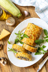 Zucchini roll with mushroom filling and herbs served on a white plate on a rustic table. Top view.