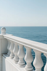 Obraz premium Marble railing overlooks the tranquil ocean under a clear blue sky. The elegant architectural detail contrasts with the vastness of the sea, offering a serene coastal view.