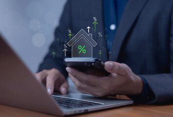 Businessman using smartphone and laptop with virtual house and percentage icon, representing real estate investment, mortgage interest rate, property finance, and digital financial technology concept.