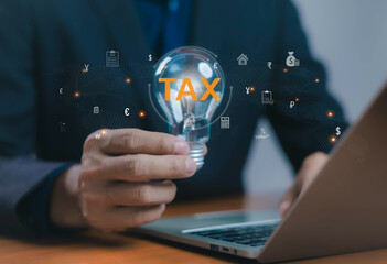 Businessman holding light bulb with TAX text and global currency icons, representing finance management, tax planning, accounting, business strategy, and digital financial innovation concept.