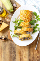 Zucchini roll with mushroom filling and herbs served on a white plate on a rustic table. Top view.