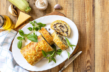 Zucchini roll with mushroom filling and herbs served on a white plate on a rustic table. Top view.
