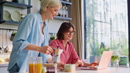 Girlfriend bringing coffee cups to working laptop woman at home kitchen closeup