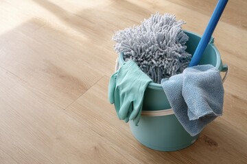 A blue cleaning bucket filled with a mop, microfiber cloths, and rubber gloves placed neatly on a light wood floor with soft daylight