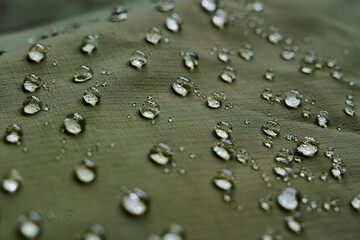 Water drops on waterproof membrane fabric. Detail view of texture of green waterproof cloth.