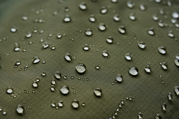 Water drops on waterproof membrane fabric. Detail view of texture of green waterproof cloth.