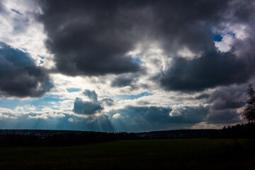 Dramatic sky with powerful, moody clouds and striking sun rays breaking through. A dark landscape silhouette completes this intense, atmospheric scene