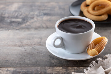Hot thick chocolate in a white cup with churros on wooden table