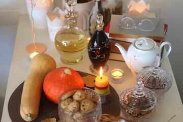 Lit candles, cookies, chocolate, nuts, tea, wine, pumpkins, books, reading glasses and autumn leaves on the table. Autumnal hygge at home. Selective focus.