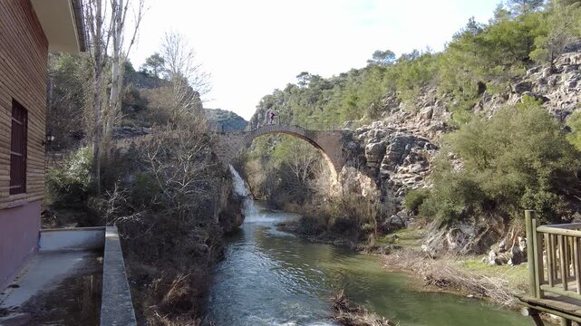 The waterfall flowing over the historical bridge offers a magnificent nature. The waterfall waters pouring under the bridge move along the river.