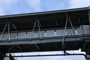 Low-angle view of a modern steel pedestrian bridge with a covered walkway, featuring metal beams and railings, set against a partly cloudy sky.