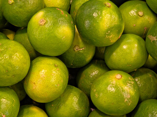 Close-up, high-angle view of a large pile of bright green limes or key limes. The fruits are tightly packed together and show some natural variations in color and texture, filling the entire frame.