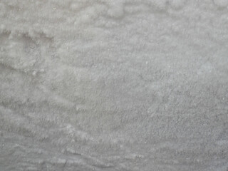 A close-up, textured abstract background of thick, white frost or ice crystals, typical of freezer burn or accumulated snow, showing slight waves and sparkling details.