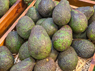 A close-up shot of a pile of ripe, dark-skinned avocados, likely in a wooden crate at a market.