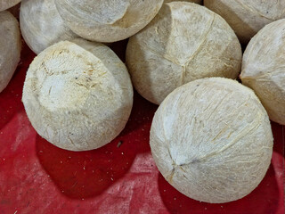 A close-up of a group of whole, white-husked, peeled coconuts displayed on a vibrant red surface.