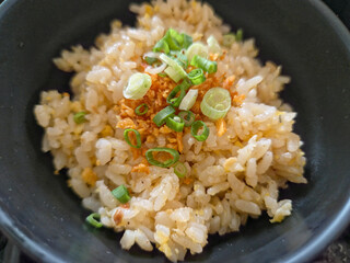 Close-up of a serving of garlic fried rice (likely Japanese or Asian style) in a dark bowl.