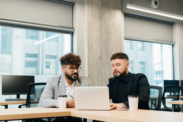 Diverse businessmen collaborating on laptop during office meeting