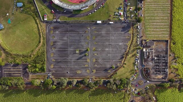 Aerial top-down view of an empty car park near a racing event area in Mauritius, surrounded by green fields and stadium grounds, captured by drone in UHD quality.