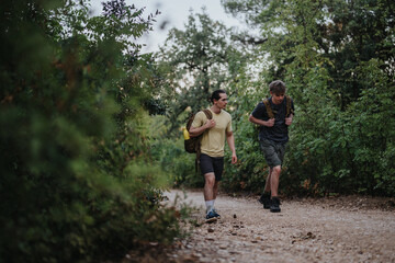 Two men hike through a leafy trail with backpacks, sharing a quiet moment in nature. The wooded path and casual clothing convey fitness, friendship, and outdoor exploration.