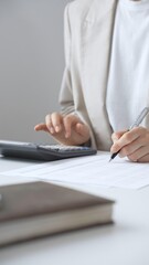 Professional businesswoman is calculating annual tax using calculator and taking notes in the...