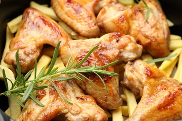 Grilled chicken wings and french fries with rosemary in air fryer basket, closeup