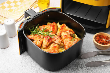 Grilled chicken wings with french fries in air fryer basket and spices on grey table, closeup