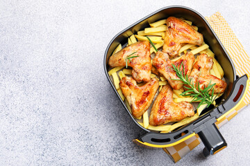 Grilled chicken wings with french fries and rosemary in air fryer basket on grey table, top view. Space for text